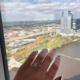 Close-up of an engagement ring with the Amway Grand Plaza in the background in Grand Rapids, MI