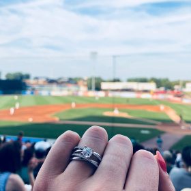 Close-up of an engagement ring with LMCU Ballpark in the background in Grand Rapids, MI